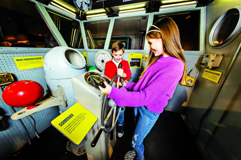 Two children play inside an interactive model of the ship&#039;s navigation bridge