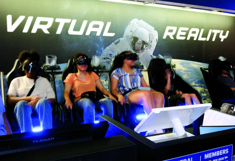 Visitors are seated and wearing goggles for a Virtual Reality experience.