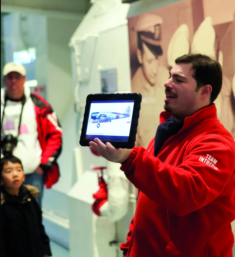 A Museum educator is showing a group of visitors a photo on an iPad.