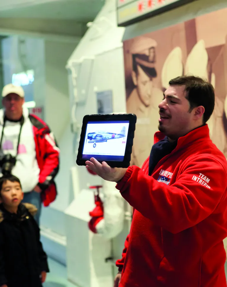 A Museum educator with an iPad showing a graphic to a group