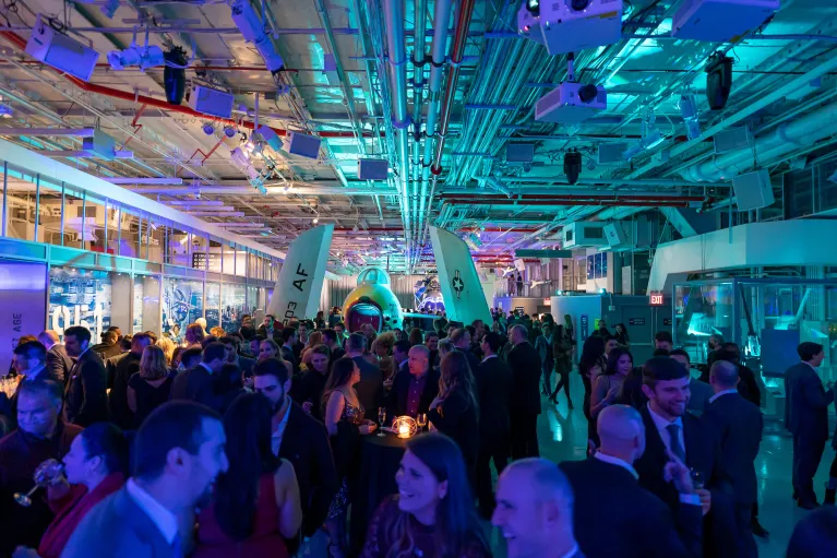 People in formal attire mingle among aircraft on the Museum&#039;s hangar deck, set with ambient lighting
