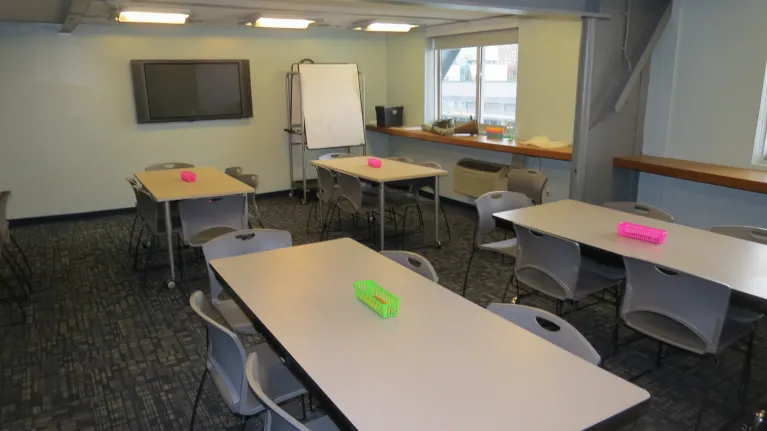 A classroom with rectangle tables and chairs around them