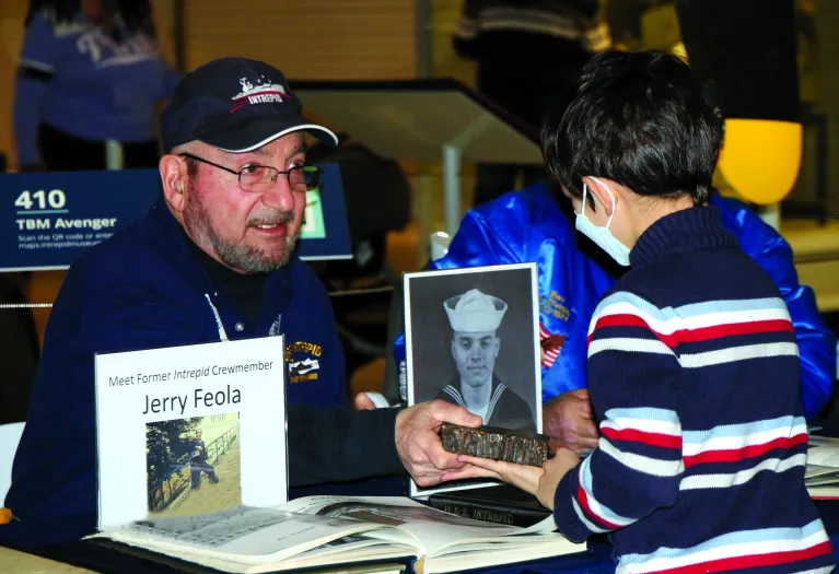A veteran is seated at a table and showing an artifact to a child.