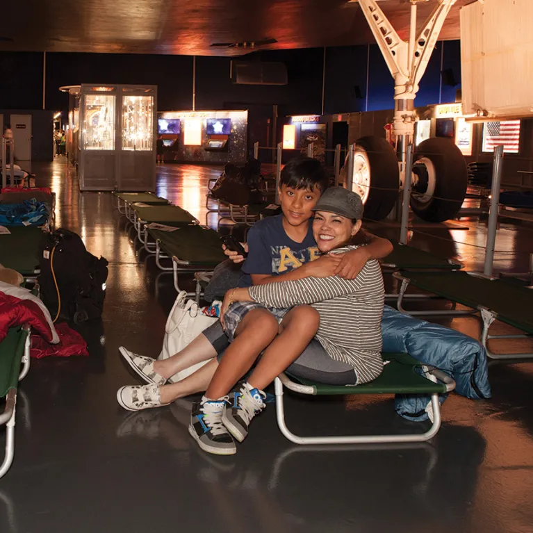 A kid and their parent are hugging while sitting on a cot on the Museum's hangar deck.