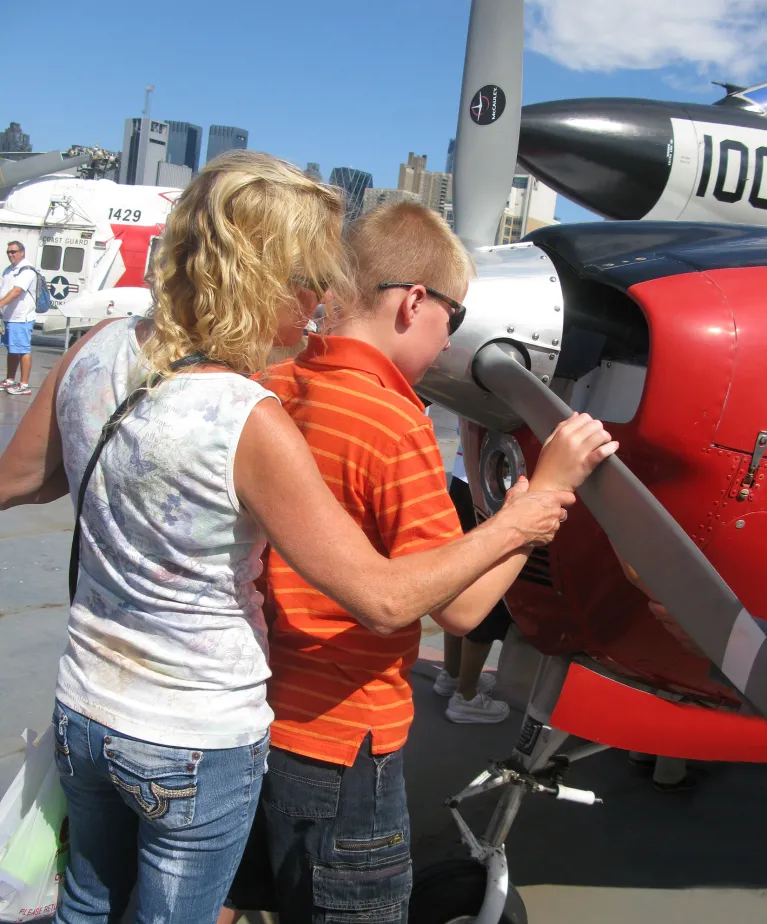 Two people are touching the propeller of an aircraft during a special event for visitors with disabilities.