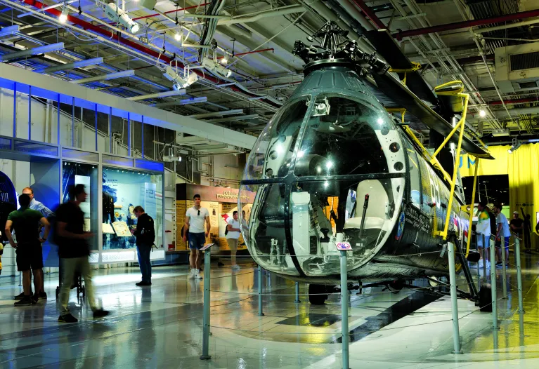 A helicopter on the Museum&#039;s hangar deck with visitors in the background.