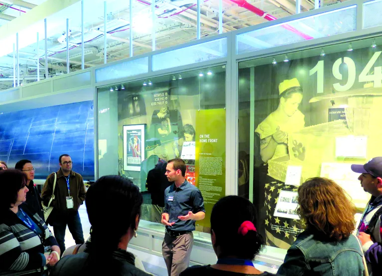 A tour guide is speaking to a group of visitors in front of an exhibition panel.