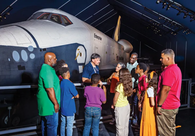 A group of visitors with a museum guide at the space shuttle pavilion.