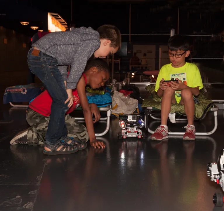 Three boys playing with a remote-controlled vehicle while attending an overnight at the Museum.