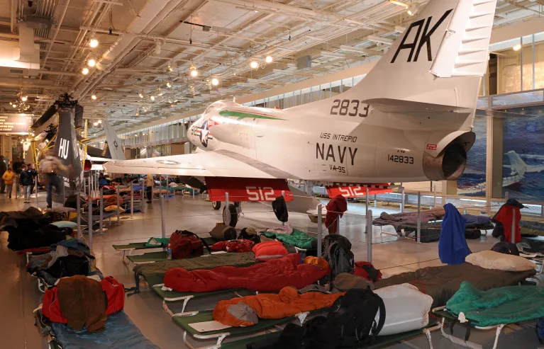 Cots and sleeping bags set up on the Hangar Deck for an overnight.