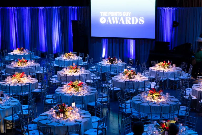 Hangar 3 seated dinner and program with blue uplighting presentation screens and floral arrangements on dinner tables