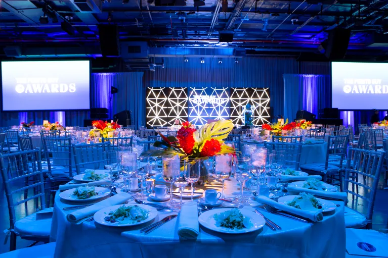 Dinner tables with florals and view of AV screens in Hangar 3 for a gala and program