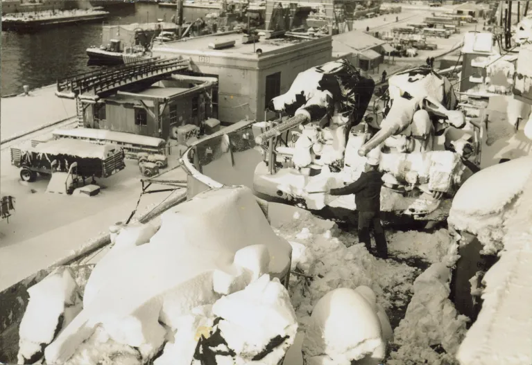 A sailor shovels snow around an anti-aircraft gun mount on Intrepid while the ship was in port, ca. 1958–1961.