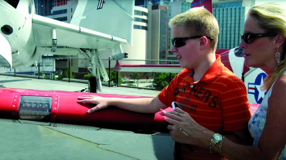 A mother looks on as her young son touches the wing of an aircraft.