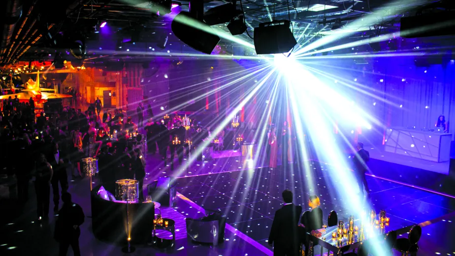 A disco ball lights up a dance floor as people mingle at cocktail tables in the Museum's hangar deck.