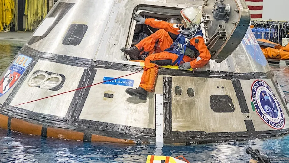An astronaut getting out of a recently water landed spacecraft at a splashdown location