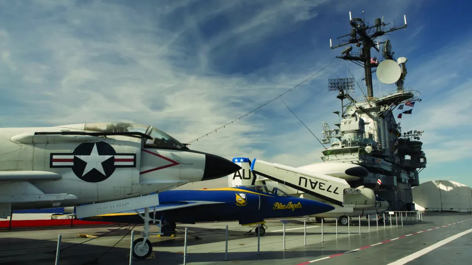 Several airplanes on the flight deck with the island and aircraft restoration hangar in the background.