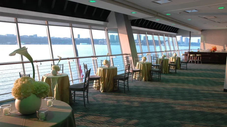 A gorgeous room with views of the Hudson River that has bistro tables and chairs set up for a special event.