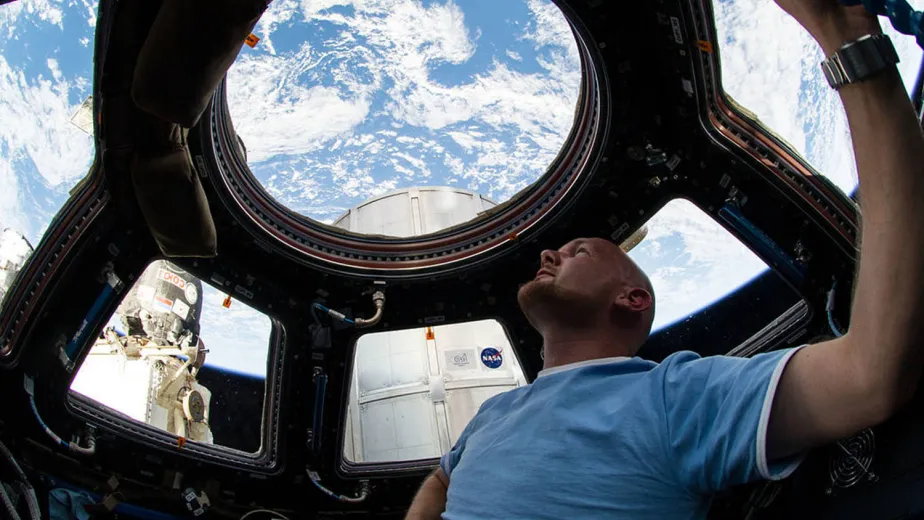 A man in a light blue shirt is in a space capsule and is looking up at a beautiful blue sky.