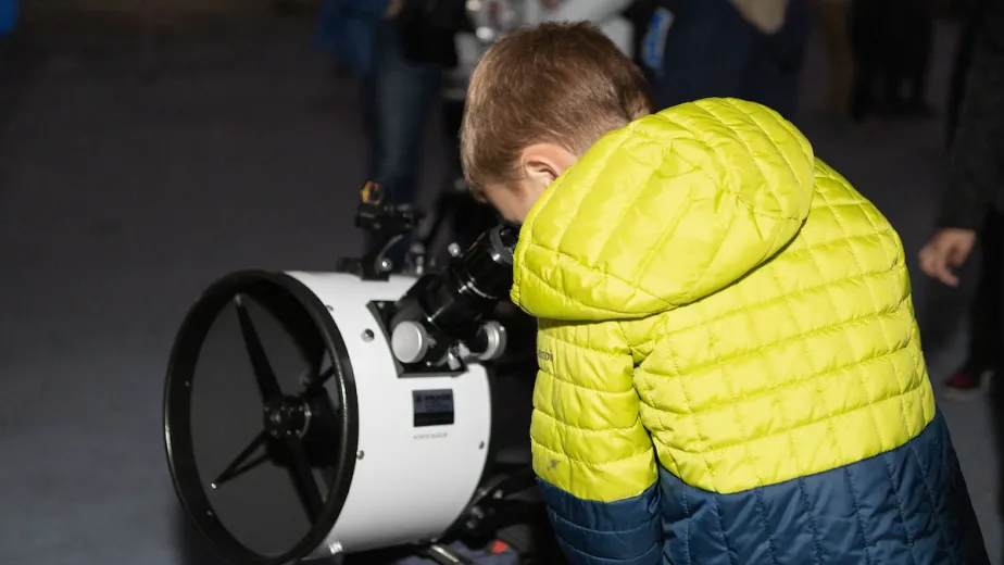 A boy is looking through a telescope.