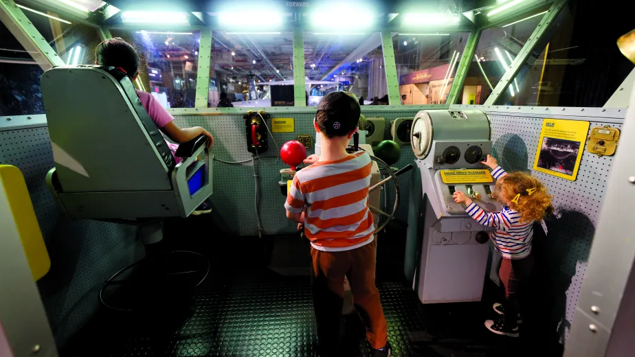 Three children playing with on a replica of a flag bridge on an aircraft carrier.