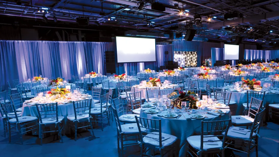 Sit down dinner venue setup with tables, screens, and stage 