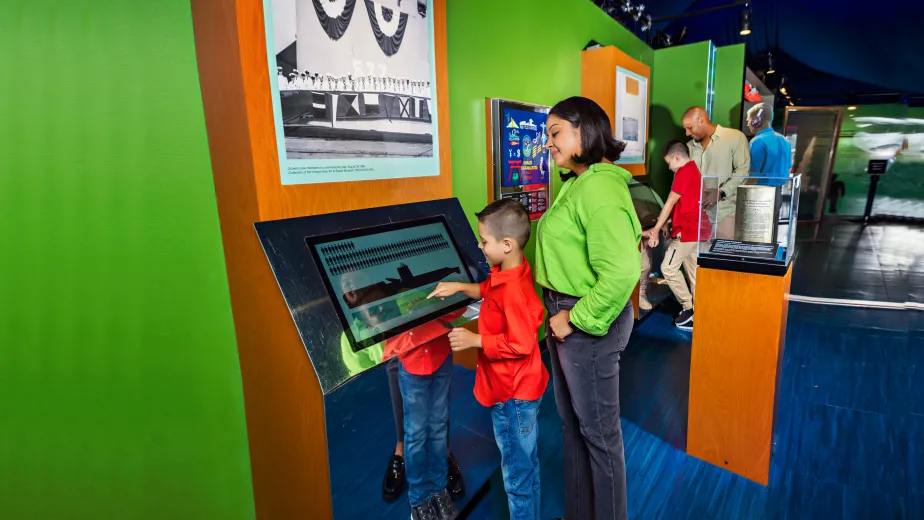 A woman and boy interact with a digital display at the view from the deep: the submarine growler and the Cold War exhibit.