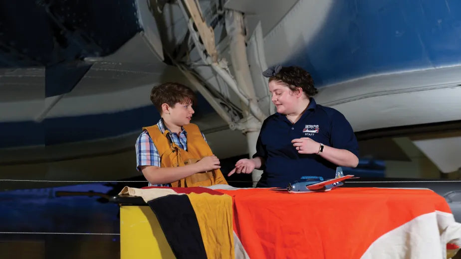 A boy wearing a Pilots floating vest with an Educator at an education station