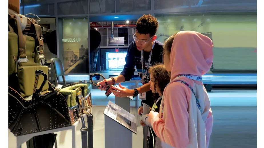 A Museum educator shows two girls how aircraft ejection seat works