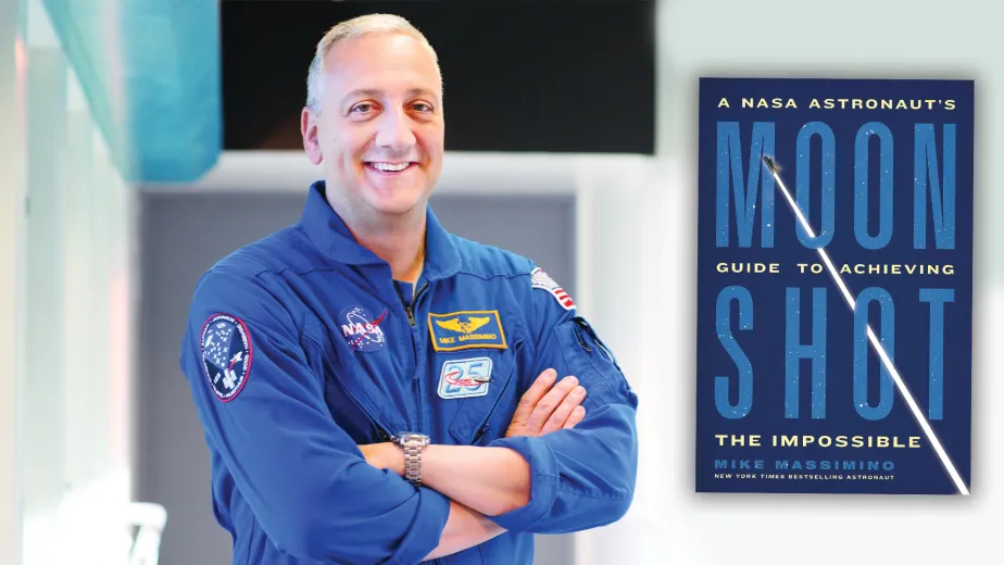 Former NASA Astronaut Mike Massimino in a space jumpsuit standing next to his new book titled 'MOONSHOT: A NASA Astronaut’s Guide to Achieving the Impossible.