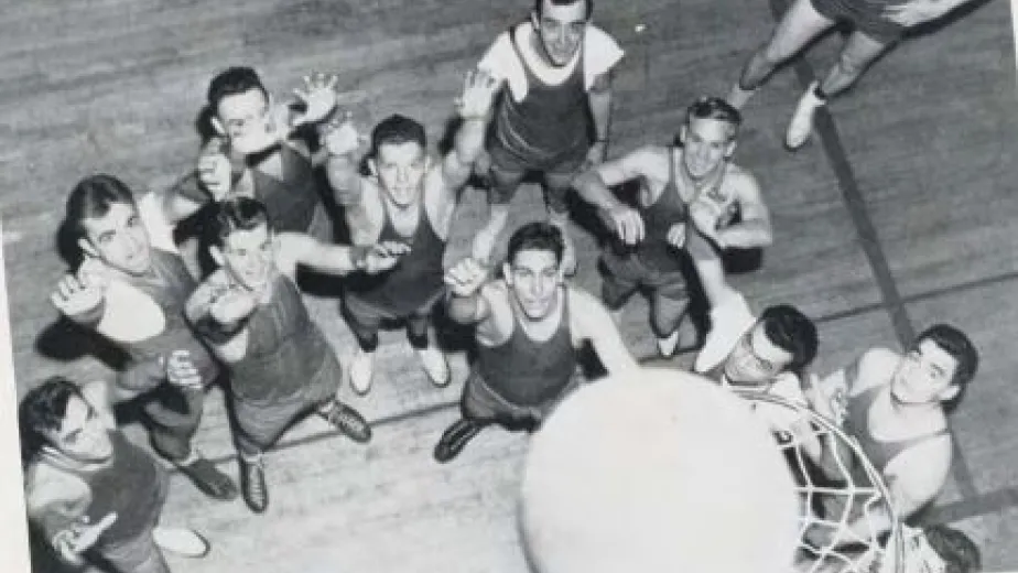 Several men are gathered around a basketball hoop, some with their hands raised. A ball is on the rim.