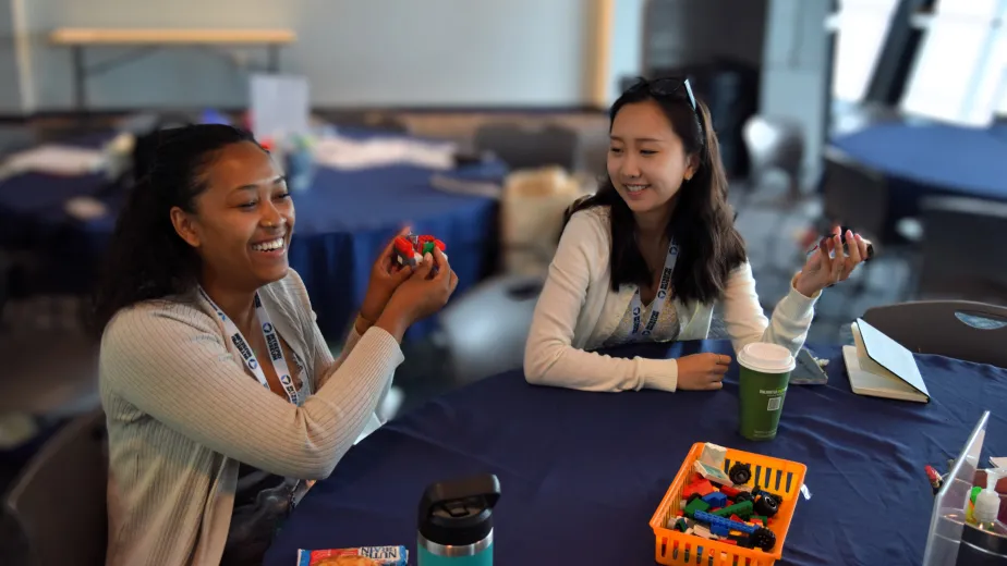 Two women seated at a round table at a conference in the Intrepid Education Center, closely examining and inspecting objects in their hands.