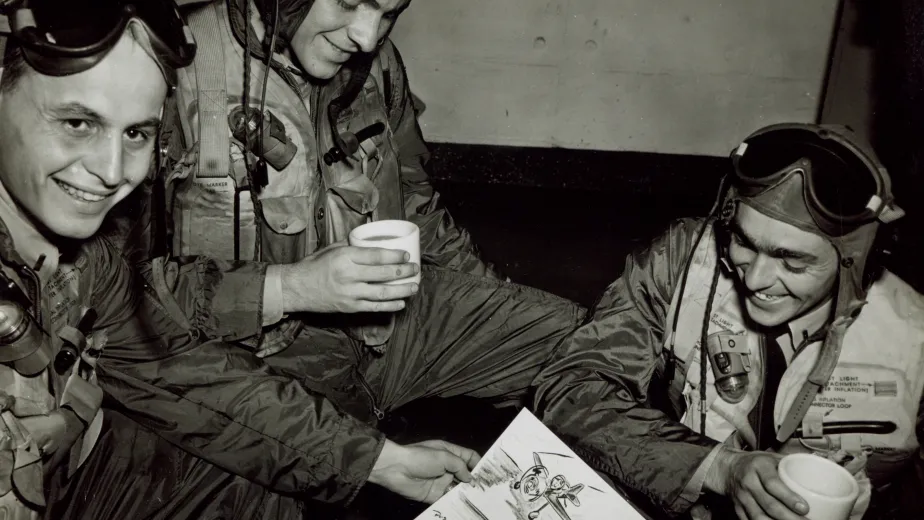 Three crew members sharing coffee while examining a sketch of fellow crew members on the flight deck.