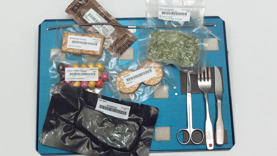 A blue astronaut food tray displaying an assortment of packaged meals and utensils