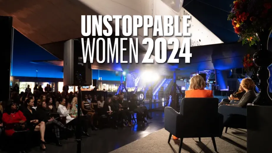 A diverse group of people seated beneath the Space Shuttle pavilion, gathered for a discussion.