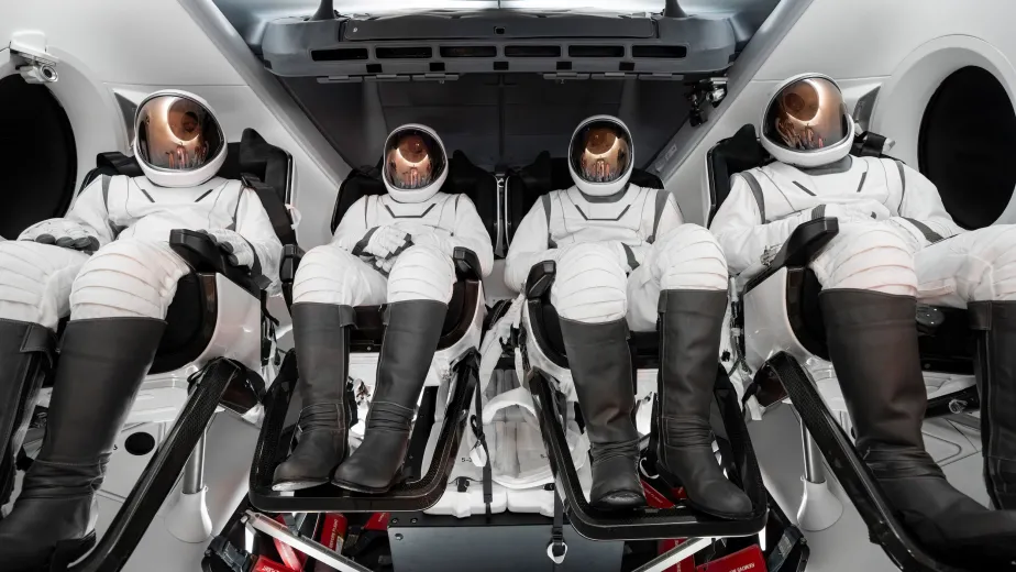 Four astronauts seated in a space shuttle wearing their astronaut suits.