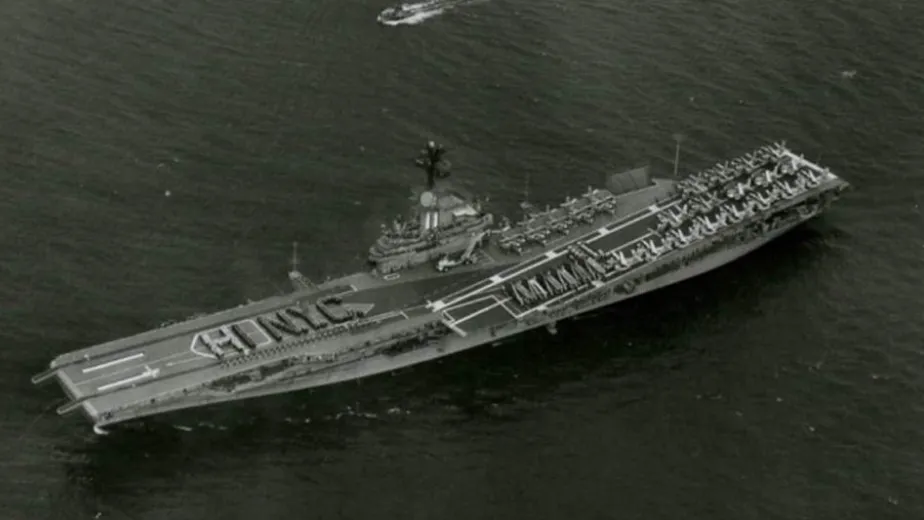 Intrepid at sea with sailors standing on the flight deck in the shape of the words, "HI NYC".