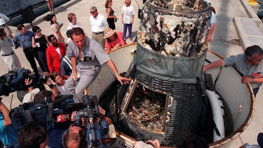 Curt Newport answering questions from the press sitting a top a space capsule.