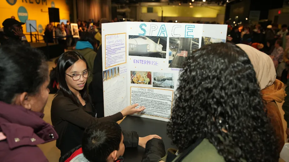 A young woman presenting a science project to several onlookers