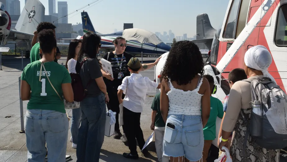 An educator leads a diverse group of children and families in exploring a helicopter on Intrepid's flight deck