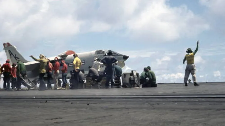 Military crew members on the flight deck guiding aircraft during takeoff and landing operations