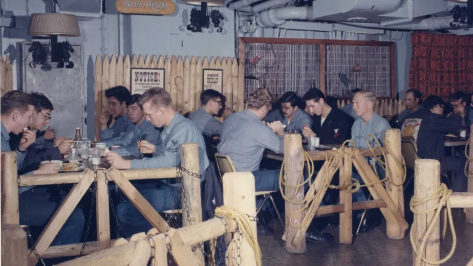 Military personnel seated on the General Mess Deck enjoying a meal and drinks