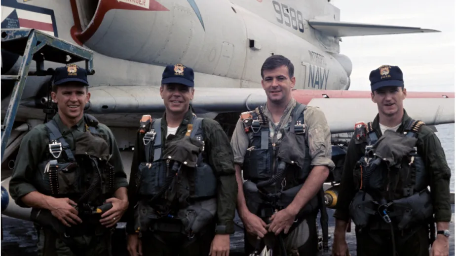 Military crew members standing on the flight deck beside aircraft.