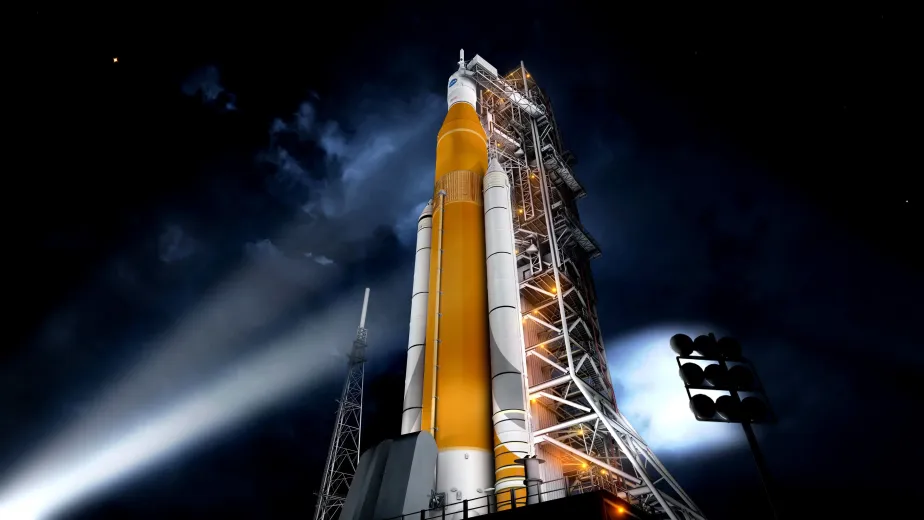 NASA’s Space Launch System rocket illuminated on the launchpad at night, with its orange core stage and white boosters beside the launch tower.