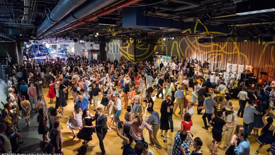 Couples swing dance to a live band in the Intrepid Museum’s hangar deck during Battle of the Big Bands.