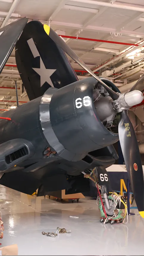 alt="Corsair aircraft inside the Intrepid Museum's hangar deck being moved into its permanent exhibition spot.