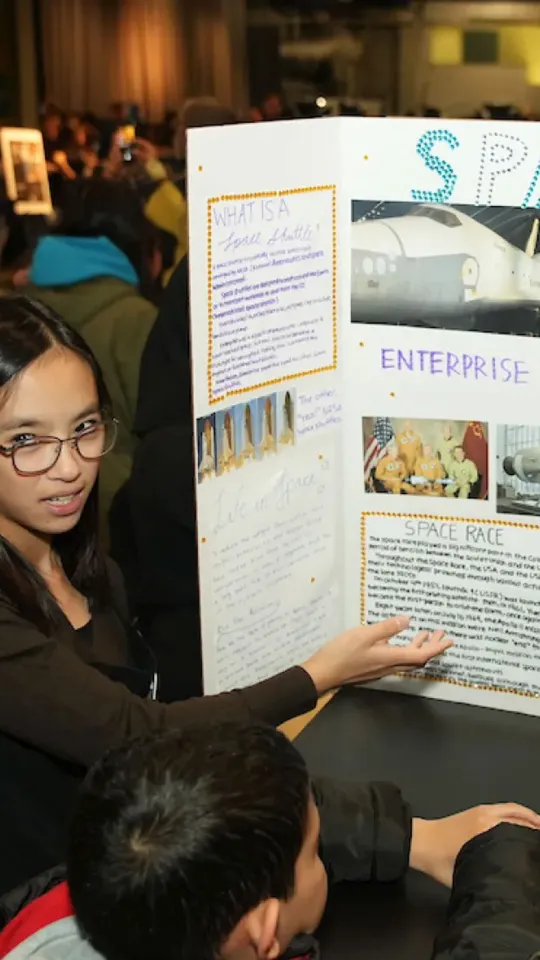 Young woman presenting her science project to a small group of attendees.